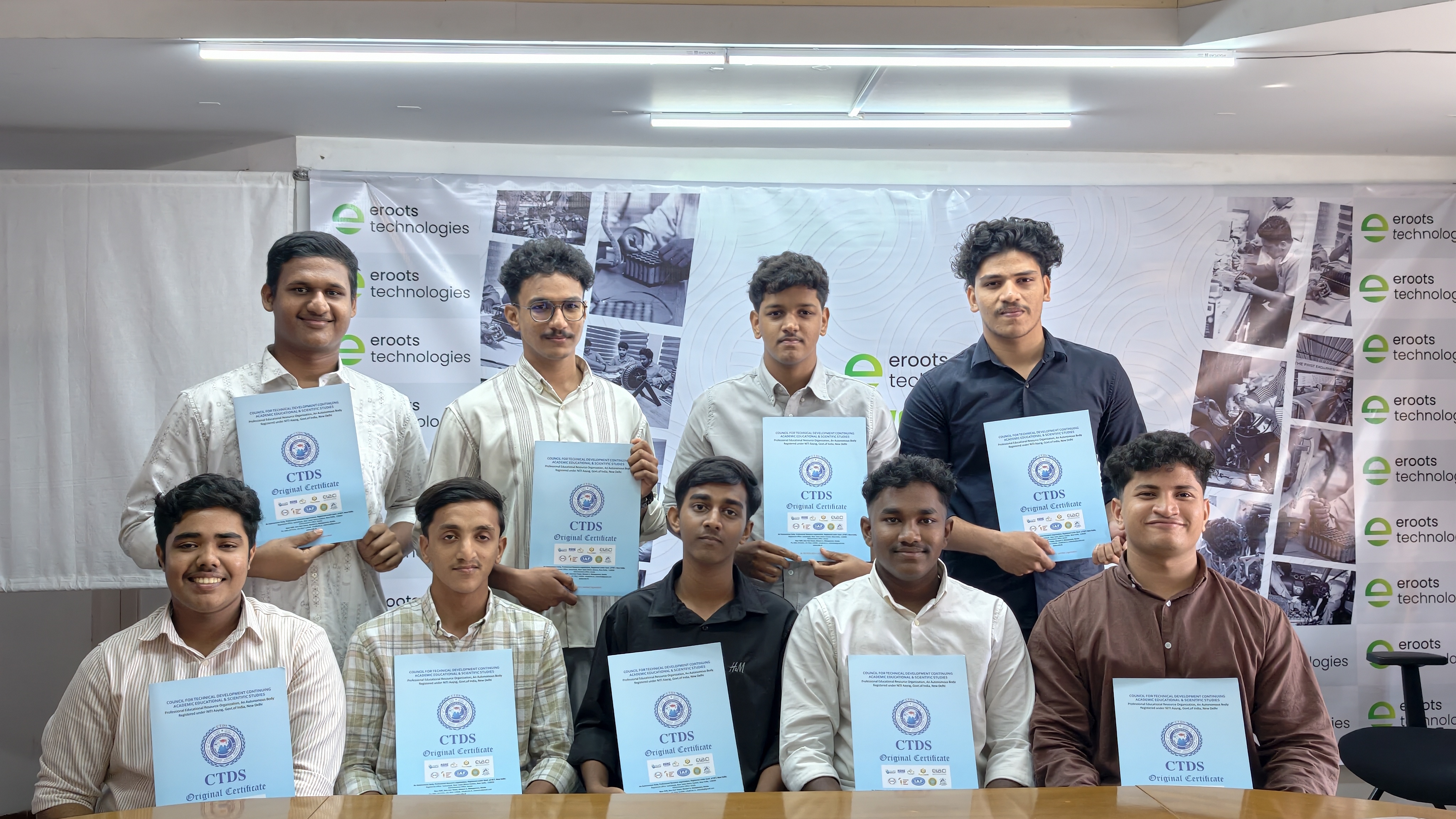 Students displaying certificates in Eroots Technologies hall.